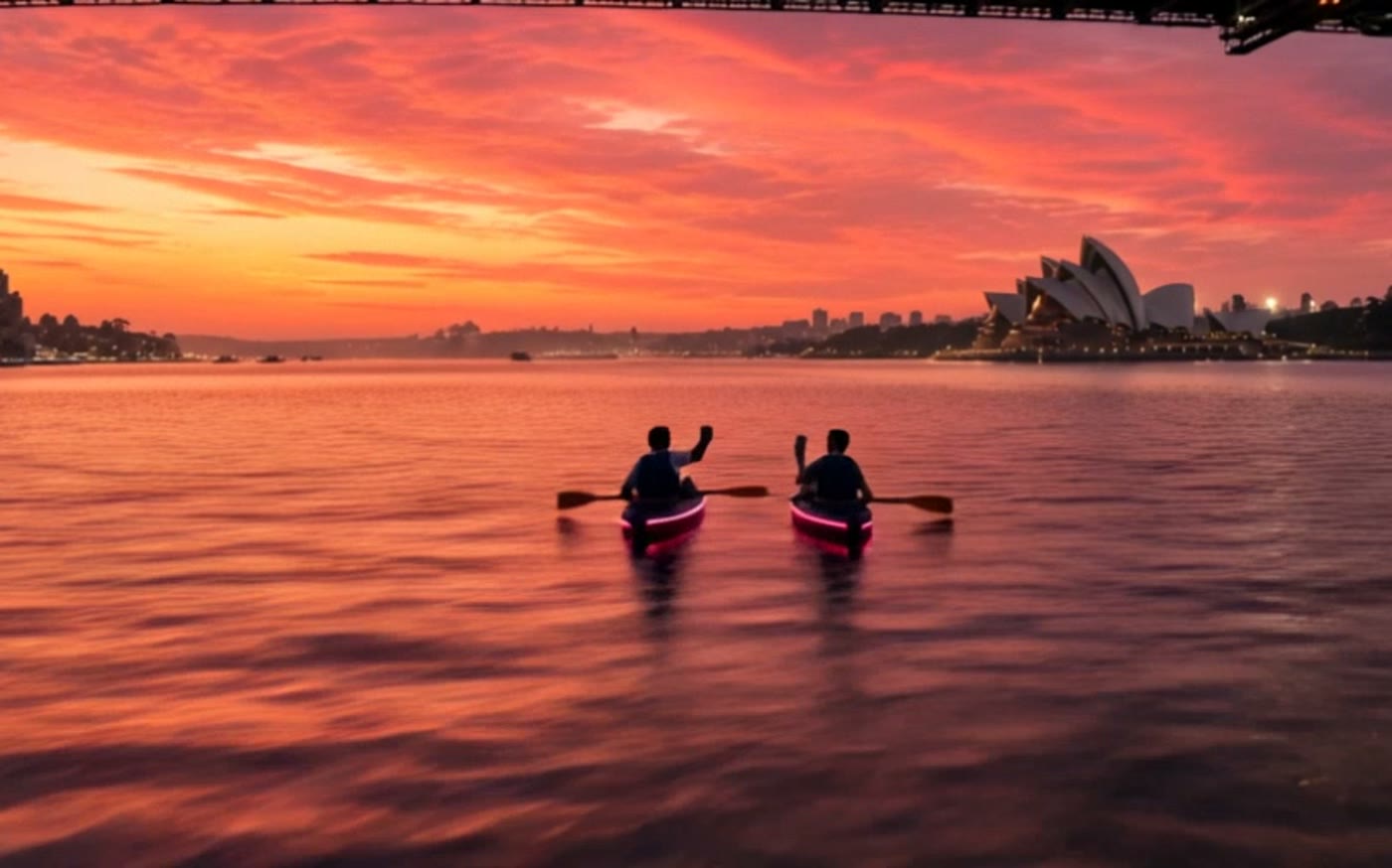 Two paddlers raise cups together on the still harbour at first light.